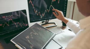 person holding tablet, and going over trade on PC screen