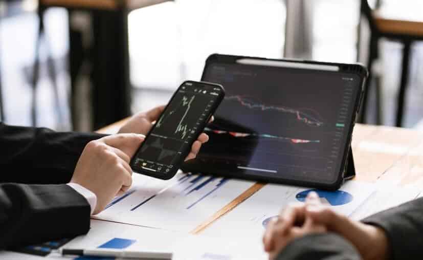 man holding phone with tablet both showing trading chart